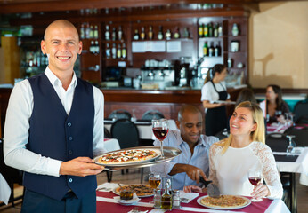 Portrait of smiling waiter in uniform with serving tray pizza at a restaurant