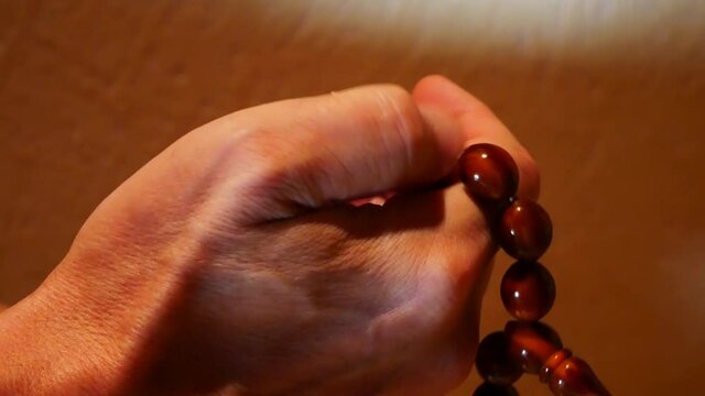 Close-up of a hand of an old man fingering brown rosary