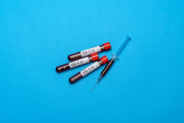 Syringe And Plastic Test Tube With Blood Sample over blue background with copyspace
