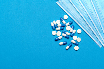Protective medical face masks and pills on a blue background - Top view with copy space