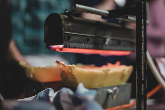 Detail of a raclette heater. Gourmet food being prepared under a gas heater above cheese.
