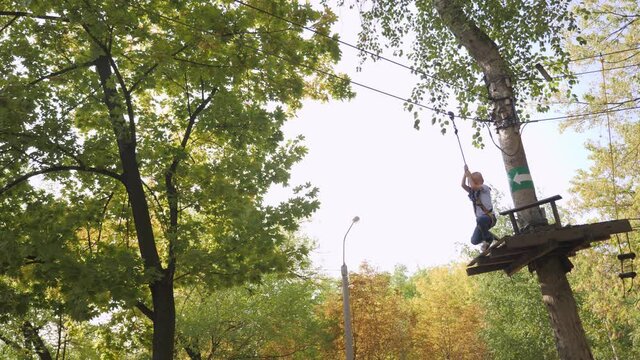 A small brave boy passes an obstacle course in a rope Park, he slides down on a zip line holding on to the rope.