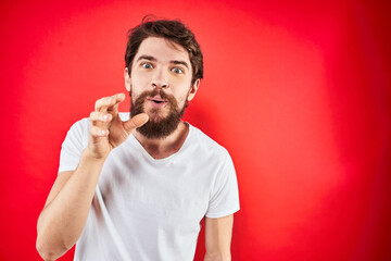 A man in a white T-shirt with a beard gestures with his hands emotions red background