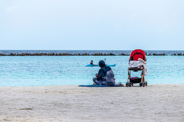 MALE, MALDIVES - Jun 29, 2018: Women feeding her child on the beach.