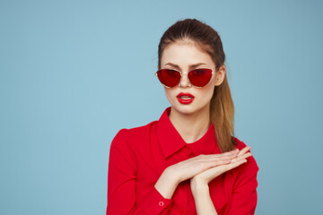 Woman in red shirt on blue background holds hands near face and sunglasses red lips makeup model