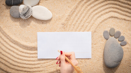 Arrière-plan grains de sable de mer, sable fin de plage avec enveloppe et coquillages. Main féminine qui écrit sur une enveloppe. Emplacement pour texte sur papier.	