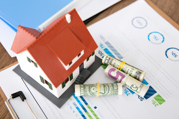 Small house model and scattered dollar bills on financial documents