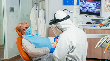Dentist doctor in coverall showing the correct dental hygiene using mock-up of skeleton of teeth during coronavirus pandemic. Medical team wearing protection suit, face shield mask and gloves.