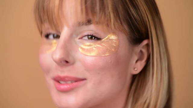 Beautiful smiling woman with short hair in gold eye patches looking in camera and smiling over colorful gold background. Beauty concept