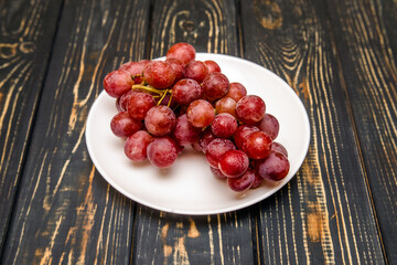 Branch of red grapes lies on a brown wooden background

