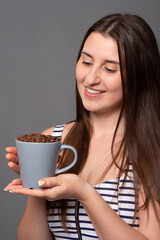 Portrait of a young woman holding a mug with coffee beans.