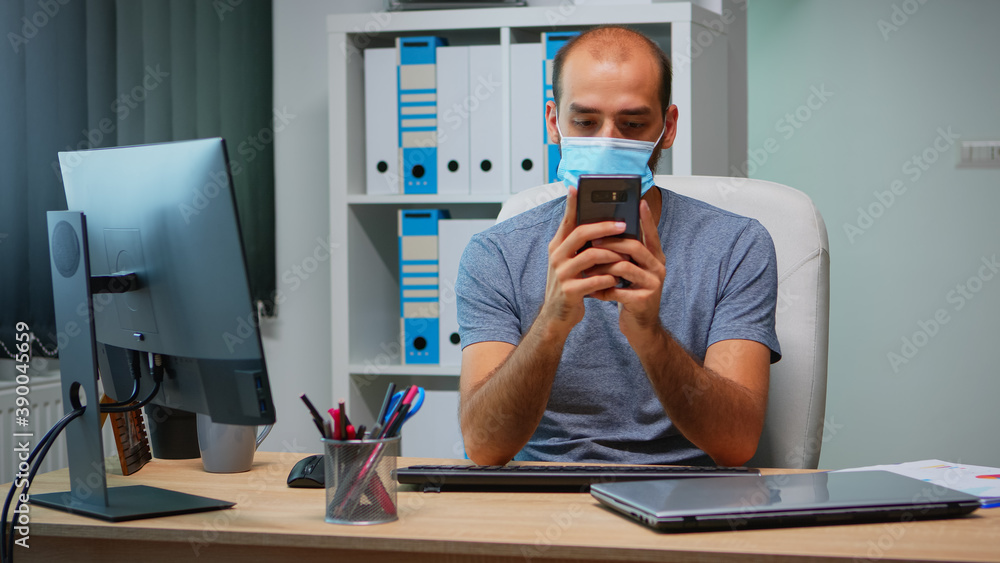 Poster office worker with protective mask using phone typing sitting on modern office during coronavirus. f