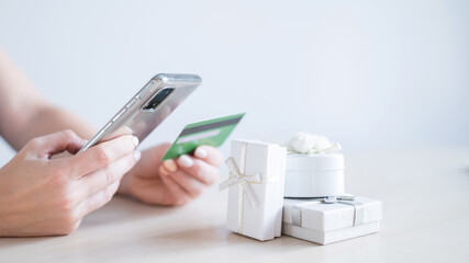 A faceless woman sits at a table and holds a mobile and a credit card in her hands. Online shopping for gifts concept