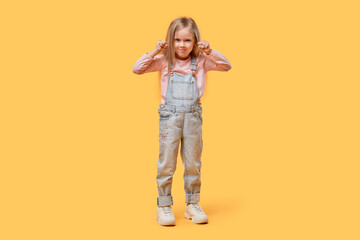 Angry girl in full growth looks at the camera. Clenched fists. Yellow isolated background.