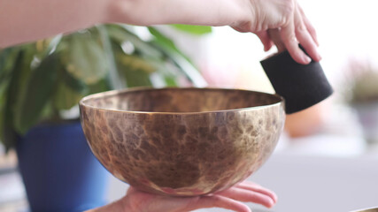 Woman playing on Tibetan singing bowl while sitting on yoga mat. Vintage tonned.