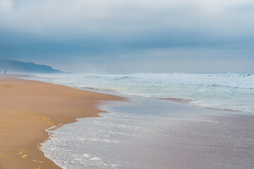 Abstract dreamlike seascape in soft blue color. Stormy ocean, sandy beach, and cloudy sky in an overcast day