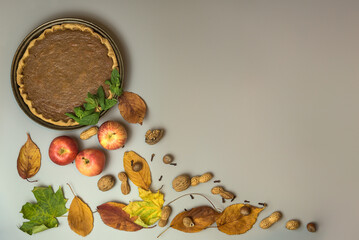 Fototapeta na wymiar Absolutely amazing Thanksgiving creative background of pumpkin pie with fresh min leaves, nuts, apples, autumn leaves, and cloves on gray background with copy space. Man cooking. Dublin, Ireland