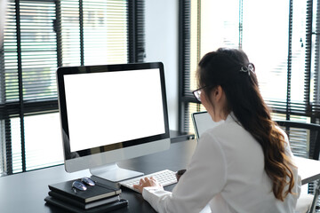 Rear view portrait of a businesswoman sitting on her workplace in the office and looking at pc...