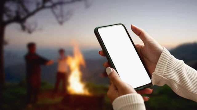 Female tourist hands holding smartphone and rest at night camping in the mountains beside campfire.