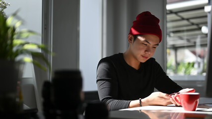 Portrait of man freelance graphic designer sitting at desk while using smart phone in his office.