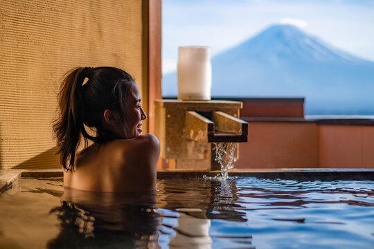 Beautiful woman enjoy onsen (mineral hot bath) in morning and seeing view of Fuji mountain in japan