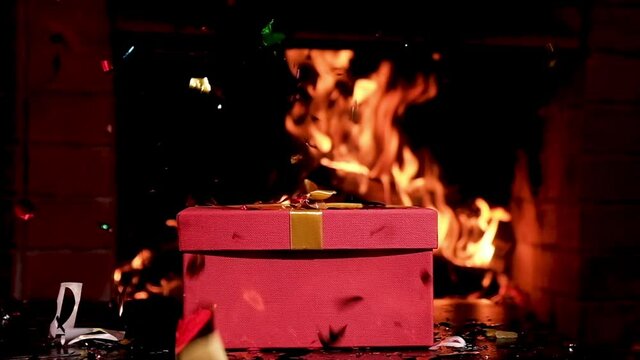 Christmas gift in large red box on table against background of fire fireplace. fun family holiday give gifts each other. Christmas weekend. Colorful candy wrappers fly around  gift.