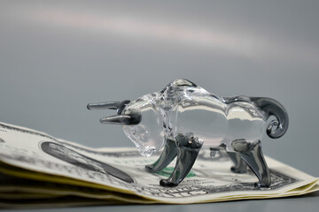 Figurine of a bull with banknotes on a gray background. Business concept, stock exchange, finance. Selective focus. US dollars are on top of each other and a glass bull standing above.