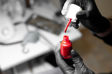 Woman's hands in black gloves hold open a jar of red nail polish. Cosmetologist's office. Personal care. Soft focus.