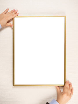 Woman hanging a frame mockup on a wall. young woman's hands hold a gold frame on a light wall background.