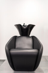 Comfortable black armchair with sink for hair washing located inside modern hairdressing salon