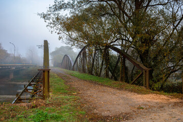 abandoned metal bridge in morning fog. dangerous construction in autumnal countryside scenery at sunrise