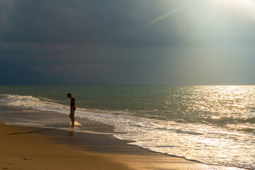 Teen boy walking on beach at sunset