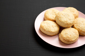 Homemade Flaky Buttermilk Biscuits on a pink plate on a black surface, side view. Copy space.