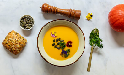 Vegan pumpkin cream soup with edible flowers, seeds and bread