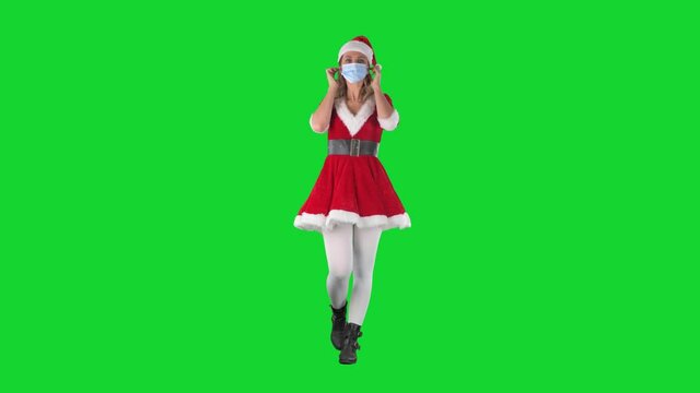 Young walking woman in Santa Christmas costume put on then remove medical face mask. Full body length on green screen background. 