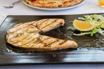 Cooked swordfish. Grilled slice of fish with lemon and salsd on plate in restaurant