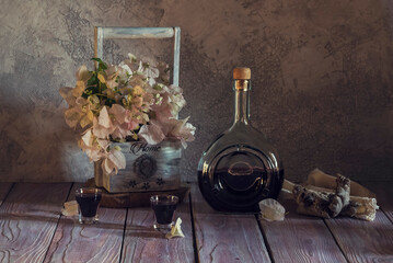 Still life with homemade liquor and a wooden basket with flowers close-up