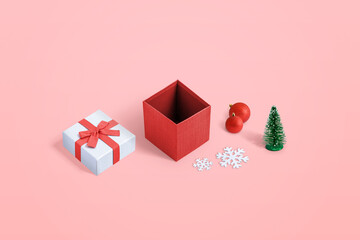 Cute opened Christmas gift box with several decorations on pastel pink background