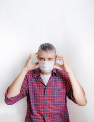 a man in a red checked shirt wears a medical mask against a white wall