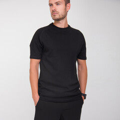 young stylish guy in black t-shirt and black pants is standing straight and looking away on the white wall background. medical concept. free space , mockup