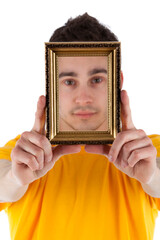 Studio photo of man with short dark hair wearing a yellow t-shirt holding a golden fram in front of face. White background.