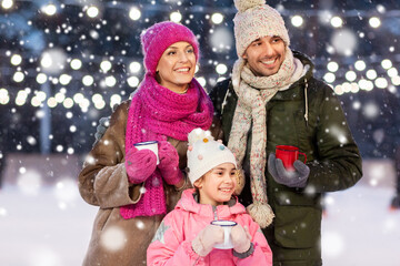 christmas, family and leisure concept - happy mother, father and daughter drinking hot tea at outdoor skating rink in winter over snow
