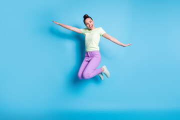 Fototapeta na wymiar Full length body size photo of young girl jumping high laughing keeping hands like plane isolated on vibrant blue color background