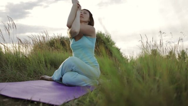 Tranquil woman meditating in Cow Face pose with Eagle arms on mat in nature while doing yoga 
