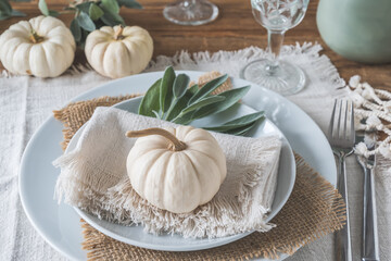 Place setting on a wooden table with white mini pumpkins, sage leaves and crystal glasses for...