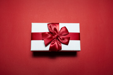Close-up of white gift box with red bow, on red background.