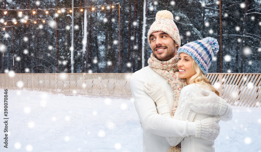 Poster winter holidays, christmas and people concept - smiling man and woman in hats and scarf hugging over ice skating rink background