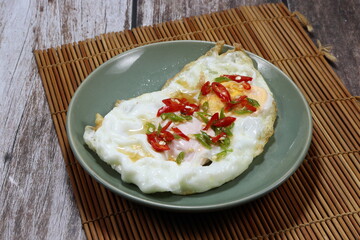 Fried fresh egg seasoning with sliced chilly and fish sauce on the plate. Famous traditional egg menu in Asia restaurant. 
