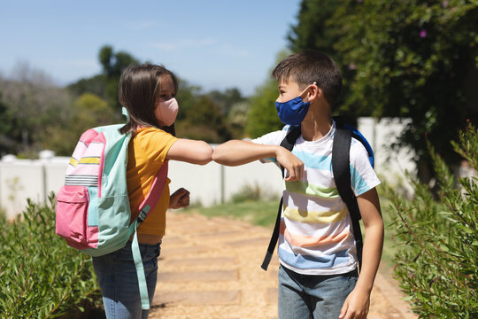 Caucasian boy and girl wearing face masks greeting on their way to school by touching elbows