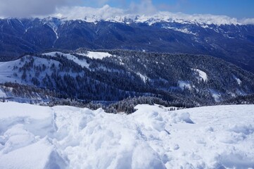 Beautiful winter landscape in the mountains, deep snow, blue sky, ski slopes, winter forest, snow-capped mountain peaks.